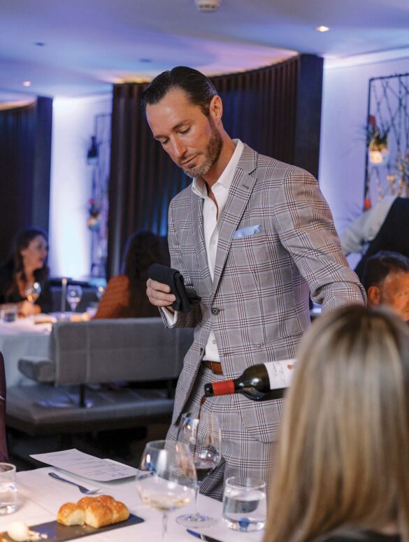 a person in a suit pouring a bottle of wine