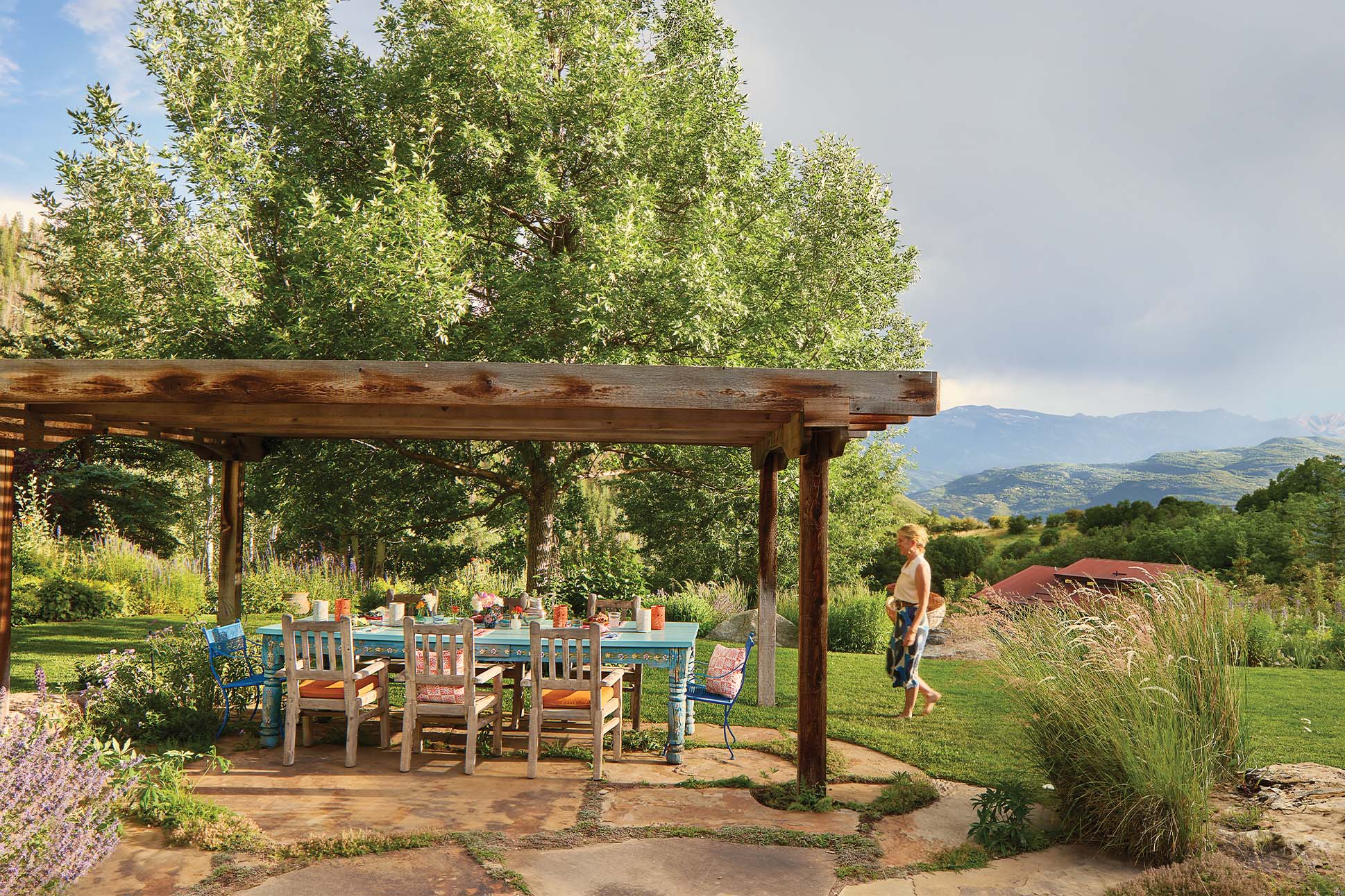 Isa Catto walks outdoors, on grass, approaching a colorful table setting under a canopy.